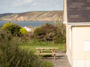 A garden with a wooden picnic table and distant hills by the sea at Bramble Cottage in Newgale