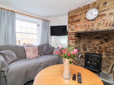 A living room with a sofa, television, and a coffee table at Willets Cottage in Appledore