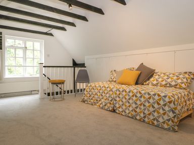 A room with a patterned sofa bed pillows a gray chair and two nested small tables near a window at Thames Reach in Wallingford