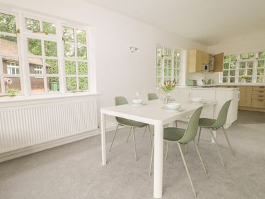 A dining area with a white table, green chairs, and a kitchen in the background at Thames Reach in Wallingford