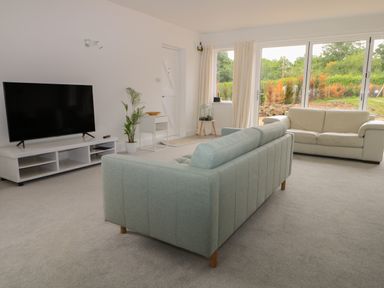 A living room with a green sofa a white sofa a large television and windows showing a garden at Thames Reach in Wallingford