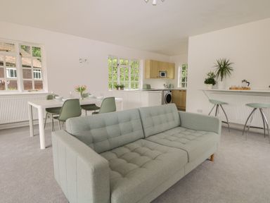 An open plan room with a sofa dining table with chairs kitchen appliances and bar stools at Thames Reach in Wallingford