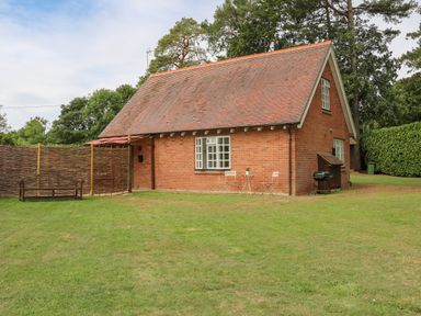 A brick house with a pitched roof in a grassy yard with a wooden bench a small table with two chairs and a barbecue grill at Thames Reach in Wallingford