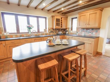 A kitchen with wooden cabinets a central island with stools cups and a teapot on the island at Ty Berllan in Caersws
