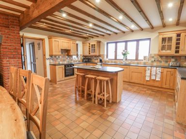 A kitchen with wooden cabinets a central island with stools tiled floor and ceiling beams at Ty Berllan in Caersws