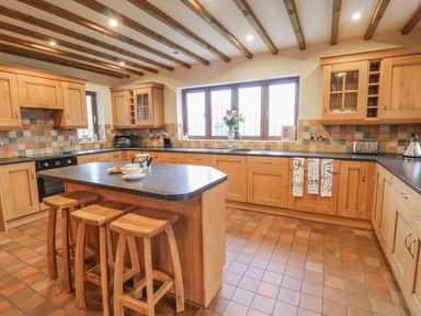 A kitchen with wooden cabinets an island with stools and a window with flowers at Ty Berllan in Caersws