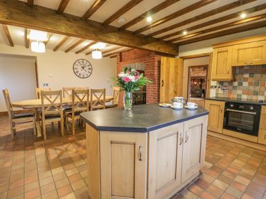 A kitchen with a wooden island counter a dining table with chairs a wall clock and exposed wooden beams at Ty Berllan in Caersws