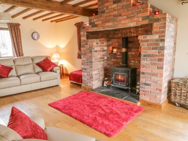 A living room with a brick fireplace leather sofas and red cushions at Ty Berllan in Caersws