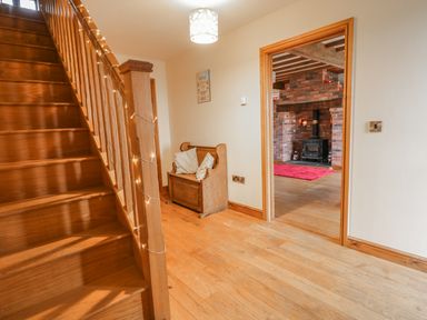 A wooden staircase with fairy lights a wooden bench with pillows and a view into a room with a brick fireplace and wood burner at Ty Berllan in Caersws