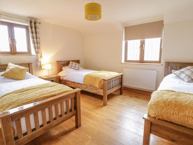 A bedroom with three single wooden beds yellow blankets and pillows and two windows at Ty Berllan in Caersws
