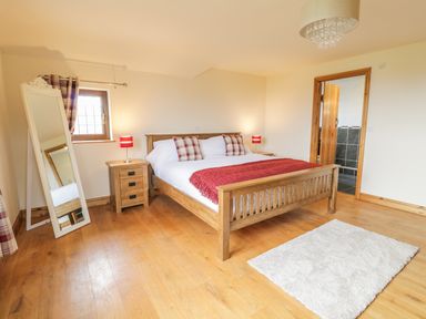 A bedroom with wooden bed frame two bedside tables with red lamps a standing mirror hardwood floor and a white rug at Ty Berllan in Caersws