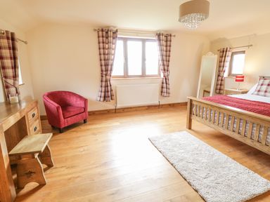 A bedroom with a wooden bed a red armchair and a wooden desk with stool at Ty Berllan in Caersws