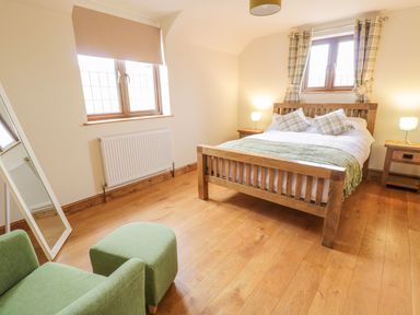 A bedroom with a wooden bed, two nightstands with lamps, a green armchair with a matching ottoman, and a full-length mirror at Ty Berllan in Caersws