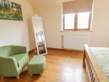 A bedroom with a green armchair and ottoman a white standing mirror a wooden bed and a window with a blind at Ty Berllan in Caersws