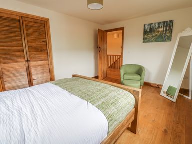 A bedroom with a wooden bed white and green bedding a green armchair a full length mirror and wooden wardrobe doors at Ty Berllan in Caersws