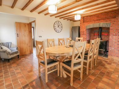 A dining room with a wooden table and chairs a brick fireplace and a wooden door at Ty Berllan in Caersws