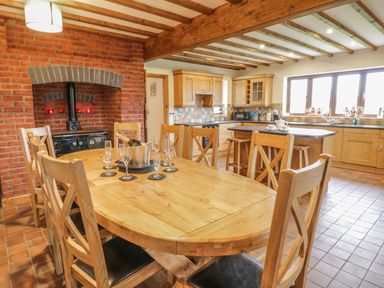 A kitchen and dining area with wooden chairs and table near a brick fireplace with a stove at Ty Berllan in Caersws