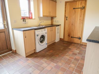 A utility room with a washing machine a sink wooden cabinets a tiled floor and a wooden door at Ty Berllan in Caersws