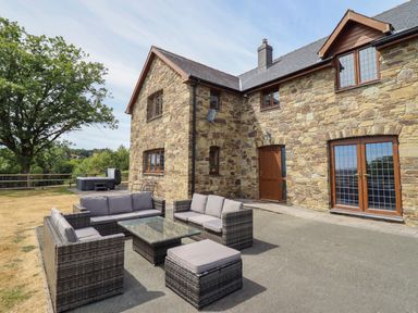 An outdoor seating area with a stone house and hot tub at Ty Berllan Caersws