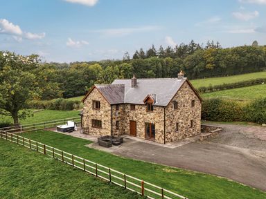 A stone house with a driveway and fenced yard at Ty Berllan in Caersws