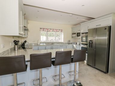 A kitchen with a large island and four stools a double door refrigerator and an oven at Ochr Y Garth in Maenan