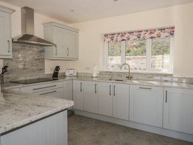 A kitchen with grey cabinets a countertop a stainless steel range hood a toaster a knife block and a window with a floral valance at Ochr Y Garth in Maenan