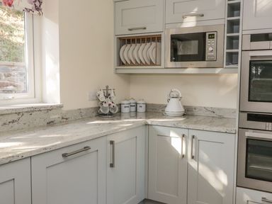 A kitchen corner with a microwave, kettle, stacked plates, cups on a stand, and containers labeled coffee sugar tea at Ochr Y Garth in Maenan
