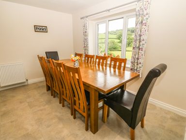A dining room with a wooden table and chairs beside a window with floral curtains at Ochr Y Garth in Maenan