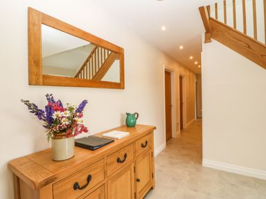 A hallway with wooden furniture and flowers on a table under a wall mirror at Ochr Y Garth in Maenan