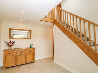 A hallway with a wooden sideboard and a mirror above it next to a carpeted staircase with wooden railing at Ochr Y Garth in Maenan