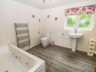 A bathroom with a bathtub toilet sink window with floral blind and a towel radiator at Ochr Y Garth in Maenan
