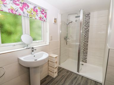 A bathroom with a pedestal sink a mirror a shower with a glass door and tiled walls at Ochr Y Garth in Maenan