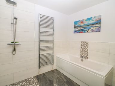 A bathroom with a bathtub shower area towel warmer and a landscape painting on the wall at Ochr Y Garth in Maenan