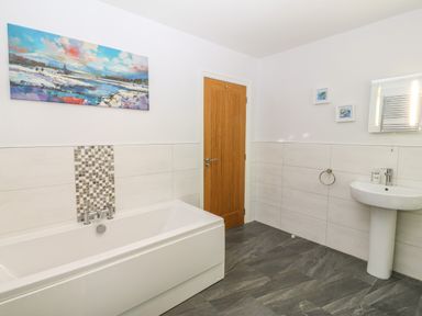 A bathroom with a bathtub a sink a wooden door and wall art at Ochr Y Garth in Maenan