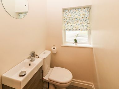 A small bathroom with a toilet sink and floral patterned window blind at Ochr Y Garth in Maenan