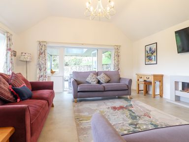 A living room with sofas a rug a wooden desk and a wall-mounted television at Ochr Y Garth in Maenan