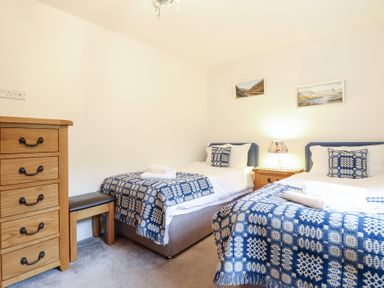 A bedroom with two single beds blue and white blankets wooden dresser and nightstand with lamp at Ochr Y Garth in Maenan