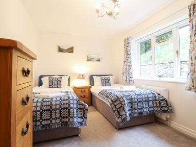 A bedroom with two single beds blue patterned blankets wooden chest of drawers and window at Ochr Y Garth in Maenan