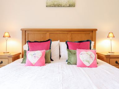 A bed with wooden headboard and colorful pillows between two bedside tables with lamps at Ochr Y Garth in Maenan