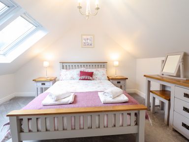 A bedroom with a bed, two bedside tables with lamps, a dressing table with a mirror, and a skylight window at Ochr Y Garth in Maenan
