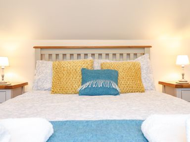 A bed with yellow and blue pillows bedside tables with lamps at Ochr Y Garth in Maenan