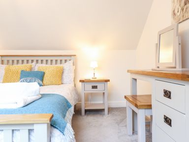 A bedroom with a bed featuring yellow and blue cushions a bedside table with a lamp and a dressing table with a mirror at Ochr Y Garth in Maenan