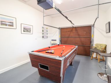 A room with a pool table and wooden chairs with a garage door in the background at Ochr Y Garth in Maenan