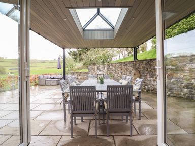 A covered outdoor dining area with a table and chairs on a stone patio at Ochr Y Garth in Maenan