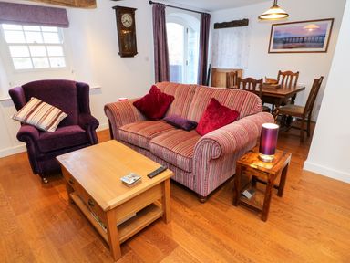 A living room with a striped sofa two red cushions a purple armchair wooden coffee table and dining table at Linden Cottage in Ravenstonedale Nr Kirby Stephen