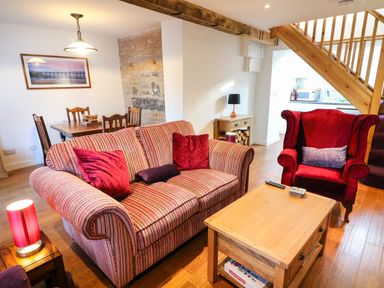 A living room with a striped sofa and red armchair near a wooden coffee table and dining table at Linden Cottage Ravenstonedale Nr Kirby Stephen