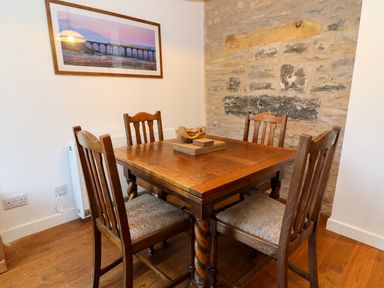 A dining area with a wooden table and four chairs against a stone wall at Linden Cottage in Ravenstonedale Nr Kirby Stephen
