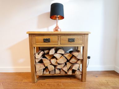 A wooden side table with firewood stacked underneath and a lamp on top at Linden Cottage in Ravenstonedale Nr Kirby Stephen