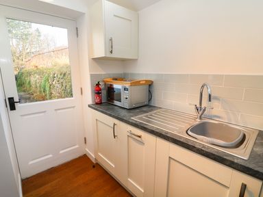 A kitchen corner with a sink microwave fire extinguisher and white door at Linden Cottage in Ravenstonedale Nr Kirby Stephen