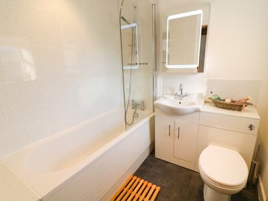 A bathroom with a bathtub shower combination a sink with a mirror above a toilet and toiletries on a cabinet at Linden Cottage in Ravenstonedale Nr Kirby Stephen